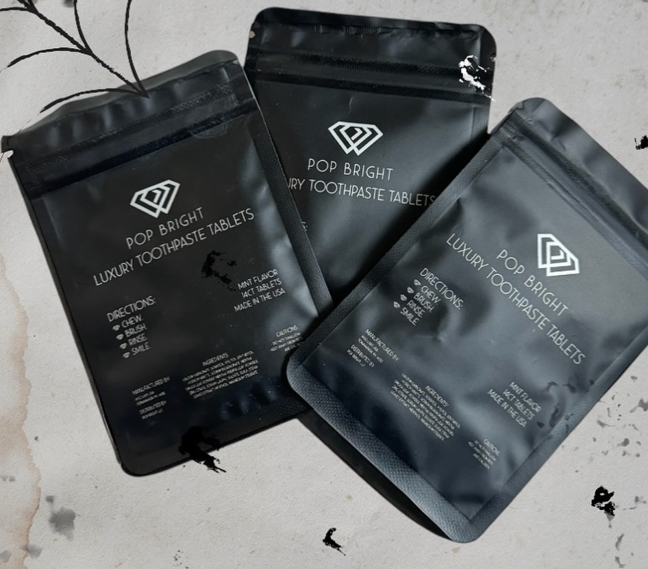 Three sleek black pouches of Pop Bright Luxury Toothpaste Tablets displayed on a neutral background with minimalist decor, showcasing eco-friendly oral care products.